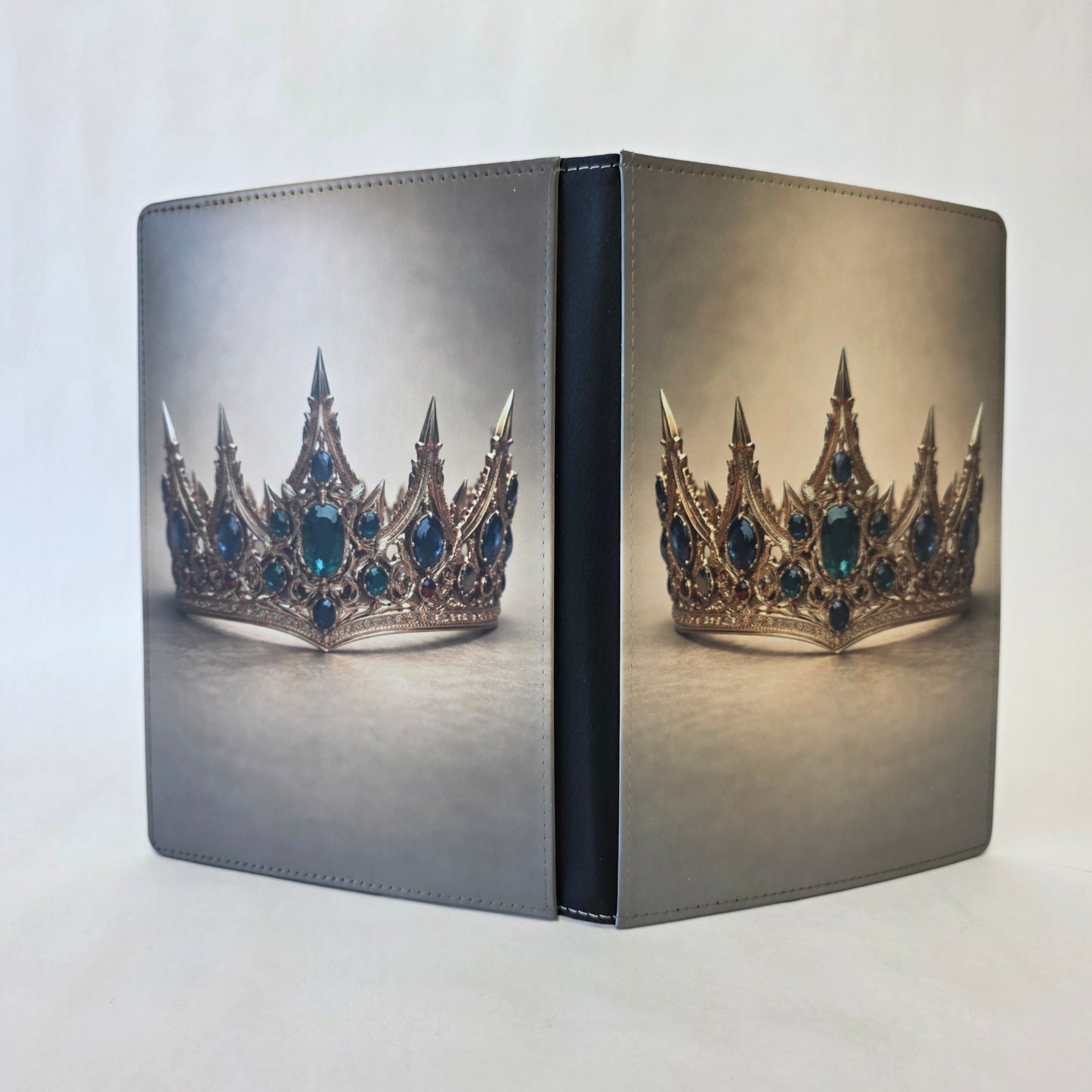 A journal cover with a gold crown and emerald stones on a tan background. Image on front and back cover.