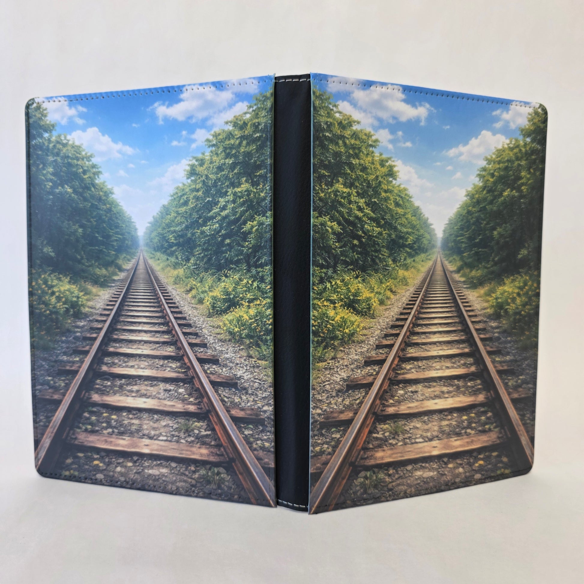 Notebook cover with a design of train tracks surrounded by trees and blue sky.