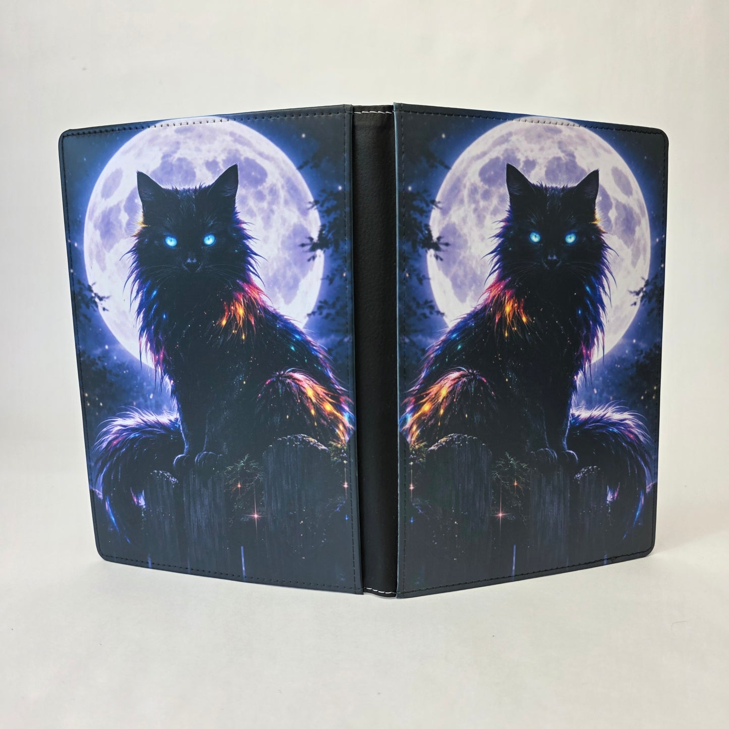 A journal cover with a black cat sitting on a fence in front of a full moon.