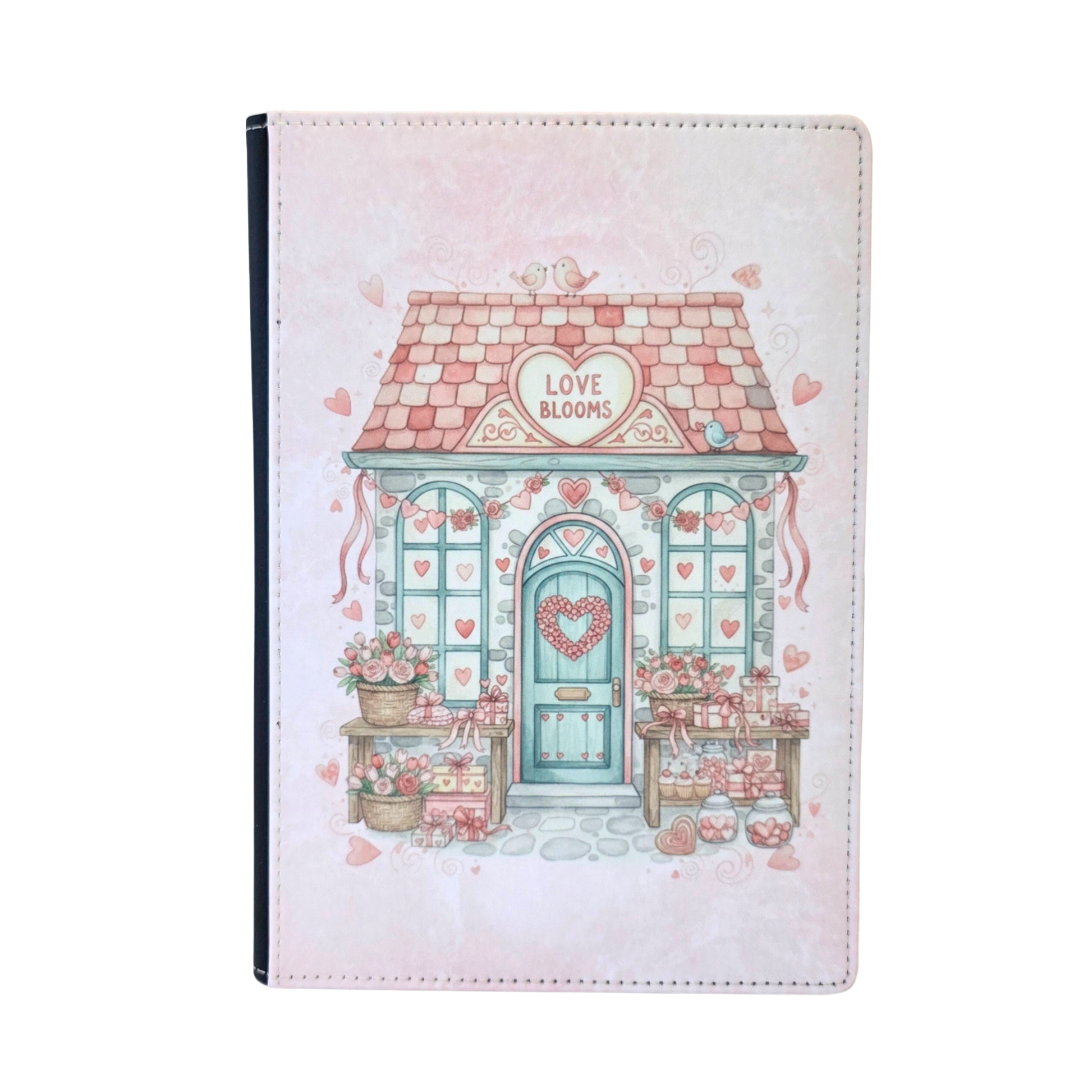 Notebook cover with a cute house illustration and 'Love Blooms' text on a heart sign above the door. Pink color theme.